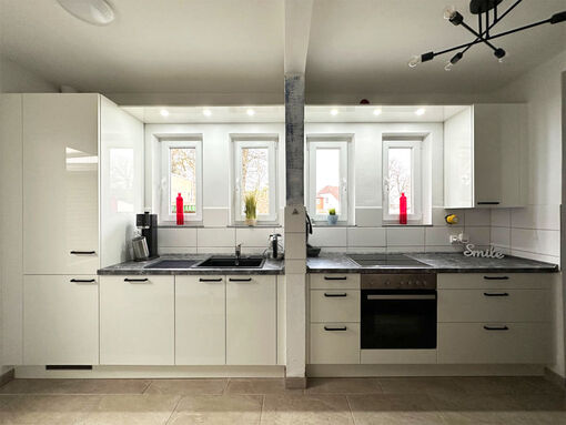 Rahmenfront in weiß Hochglanz; APL: Luna dunkel, Baubedingt ist die Küche in zwei Bereiche getrennt: Spülbereich mit einteiliger großer Spüle und Türen und Kochbereich mit großen Auszügen und eingebauter Beleuchtung im Abdeckboden 