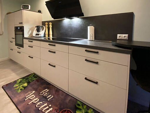 Moderne, zweizeilige Küche mit Satin matten Fronten, APL: Spachtelbeton graphit. Der Geräteschrank in Highboard-Höhe, die elegante schwarze Kopffrei-Haube und das große Kochfeld ermöglichen ein unbeschwertes Arbeiten | Küchenhaus Kunz